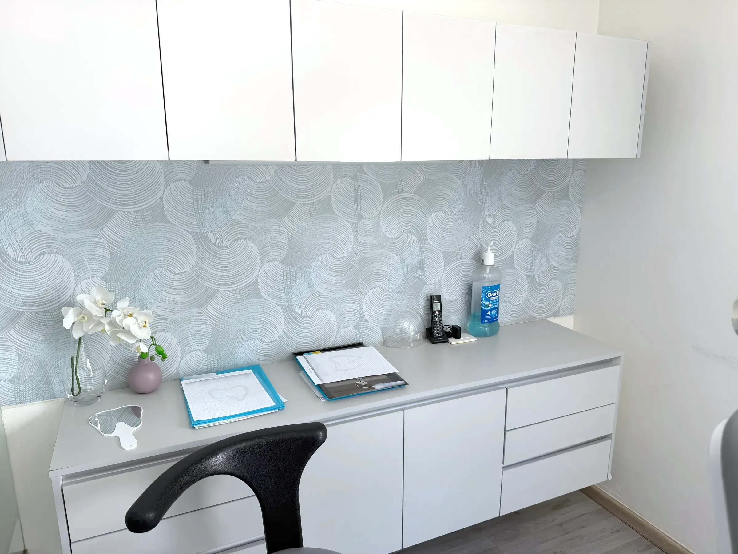 Mueble de trabajo de un consultorio con papel tapiz texturizado y orquídeas blancas.