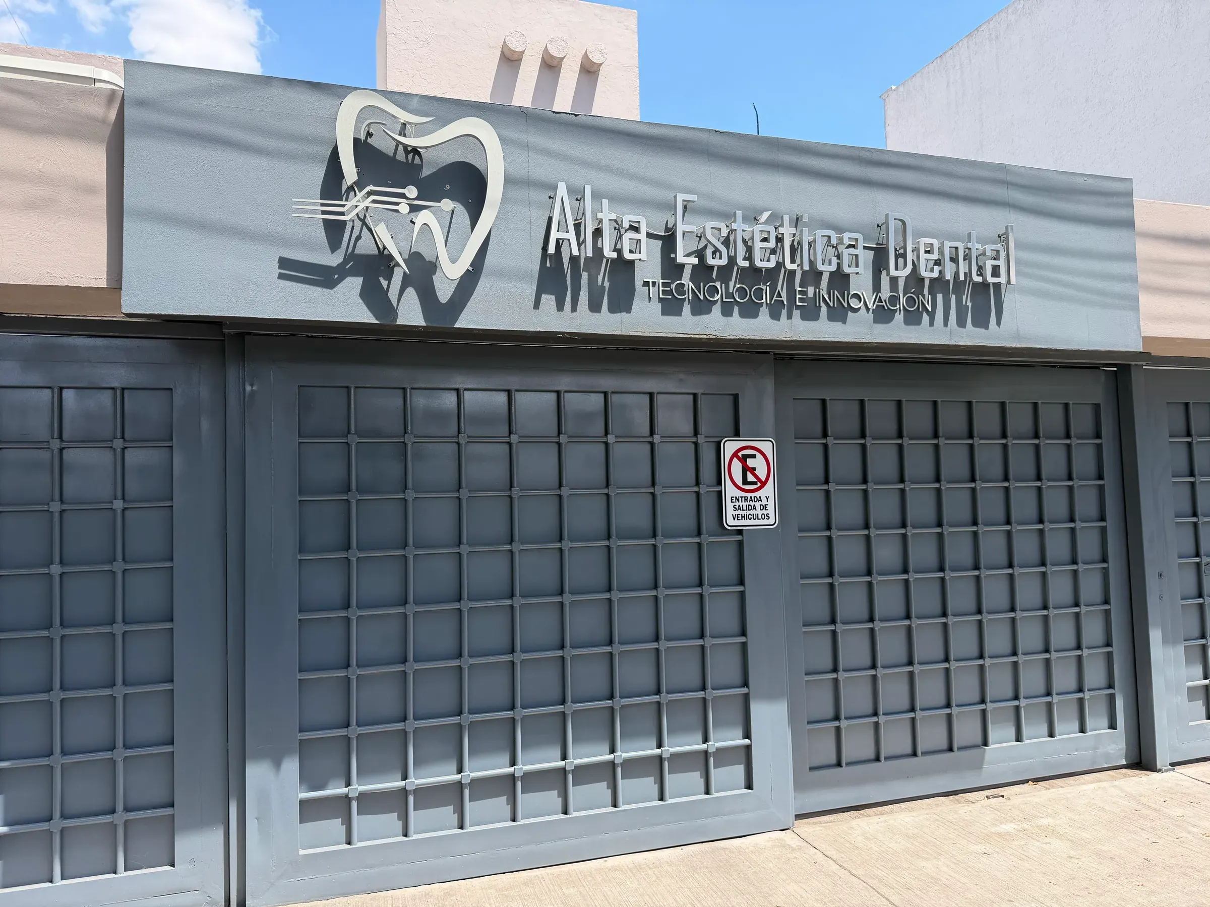 Fachada de Alta Estética Dental: letrero con el logotipo sobre los portones grises.