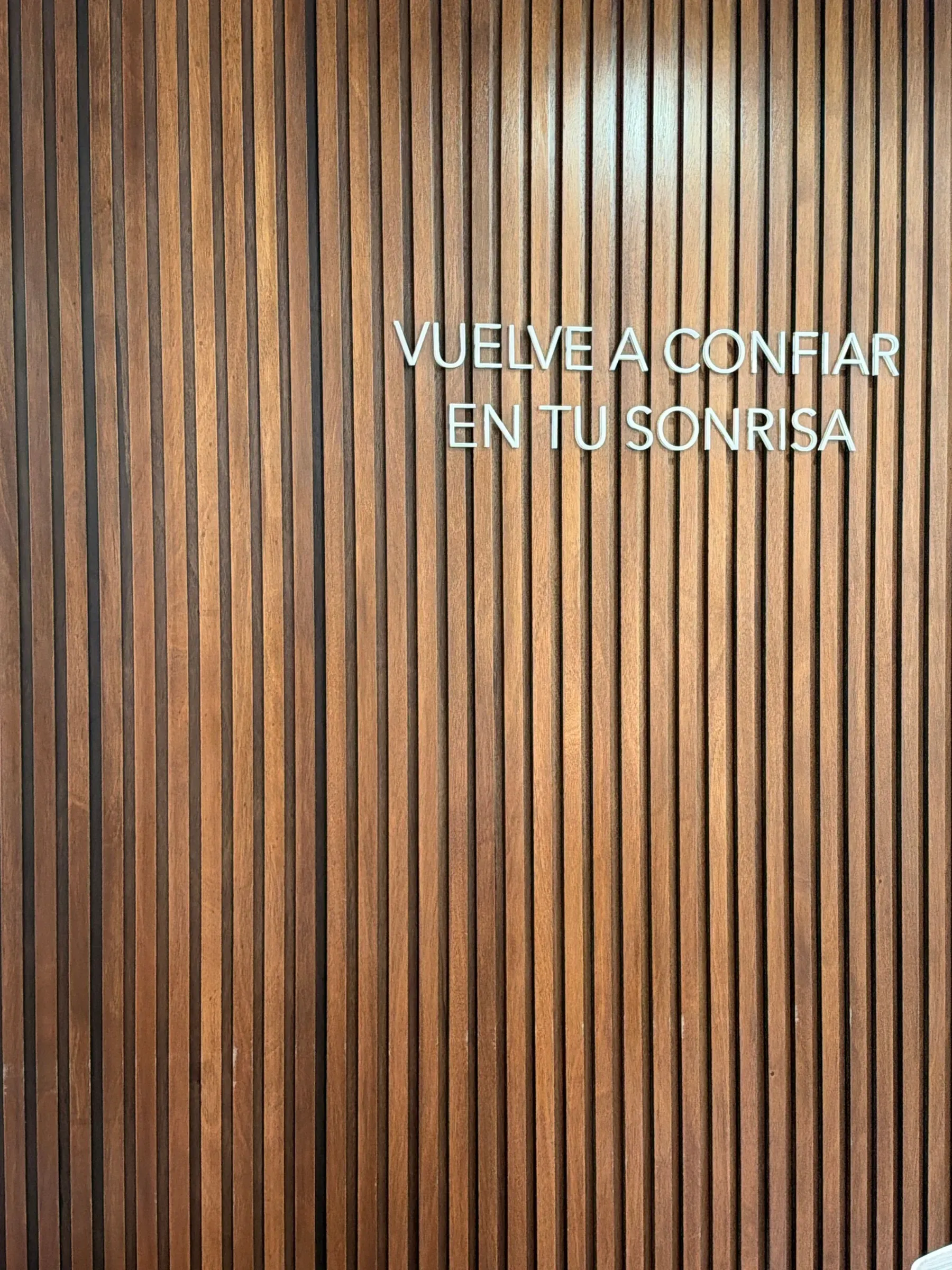 Muro de listones de nogal con la frase «Vuelve a confiar en tu sonrisa».