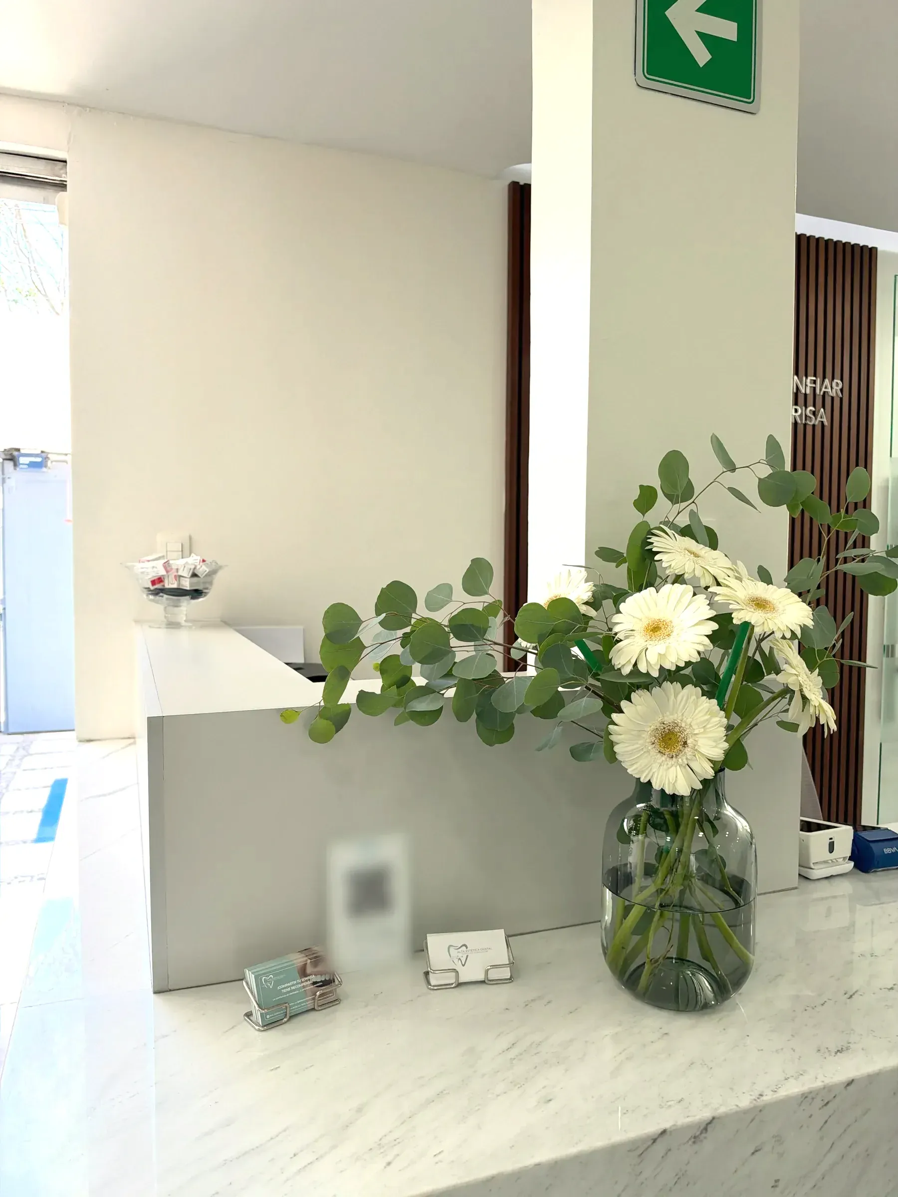 Mostrador de recepción de mármol con flores blancas y el muro de madera al fondo.