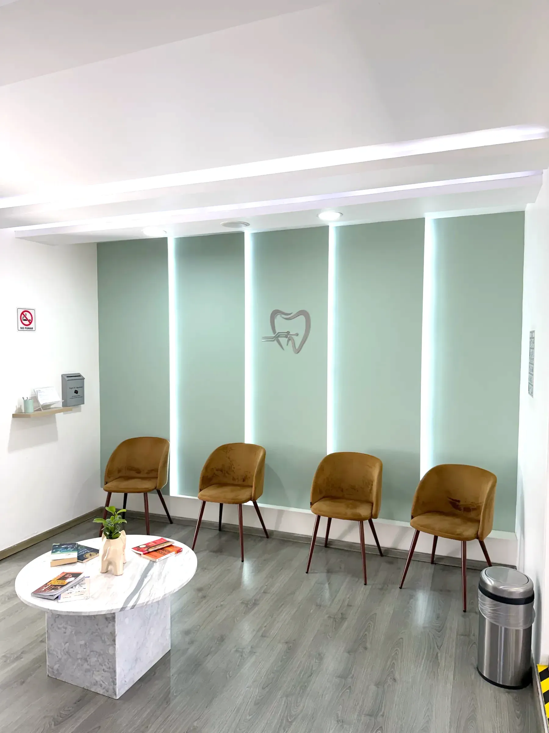 Sala de espera con paneles verde salvia retroiluminados, sillas color cobre y mesa de mármol.