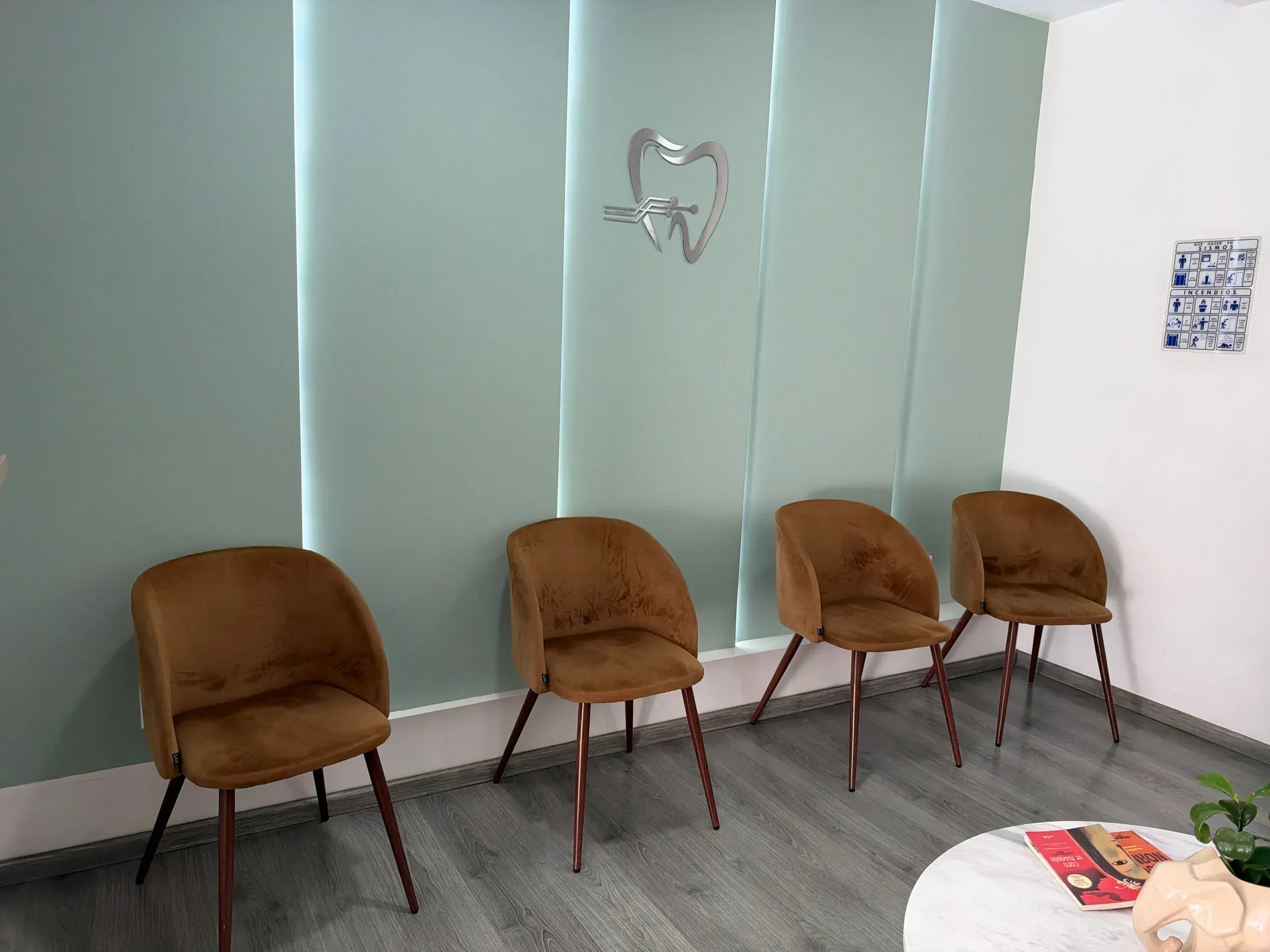 Sala de espera con paneles verde salvia retroiluminados, el emblema de la clínica y sillas color cobre.
