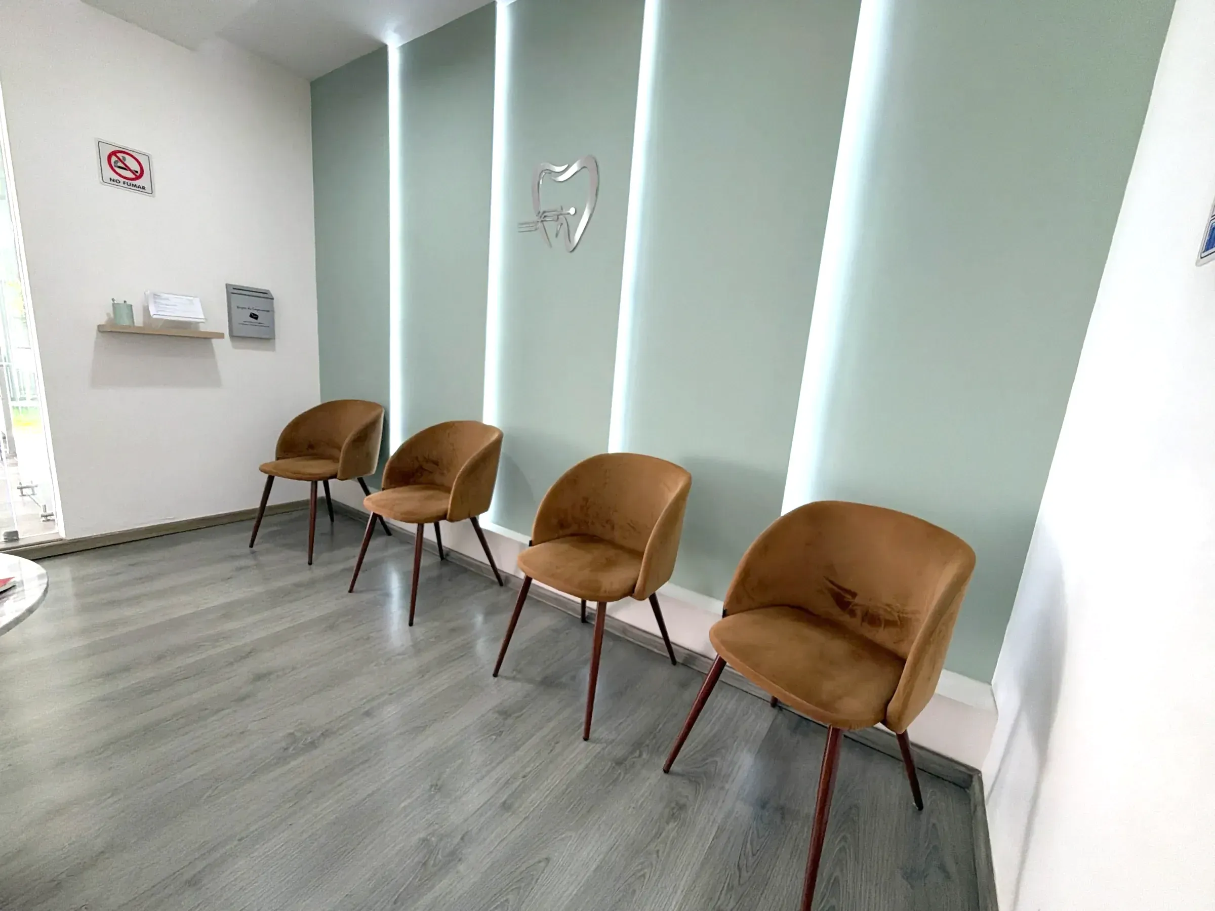 Sala de espera con paneles verde salvia iluminados y sillas color cobre.